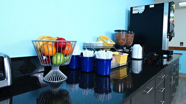 Un piano di lavoro in cucina con una ciotola di frutta, contenitori per condimenti e una macchina da caffè.