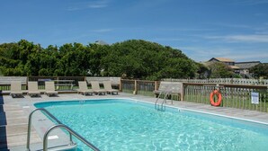 Ein rechteckiger Pool mit Holzdeck und Metallleiter, umgeben von einem Holenzaun und Bänken.