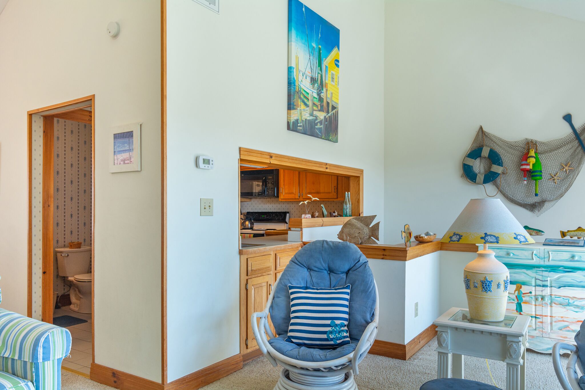 A cozy living room with a blue armchair, a wooden cabinet, and a painting of a coastal scene.