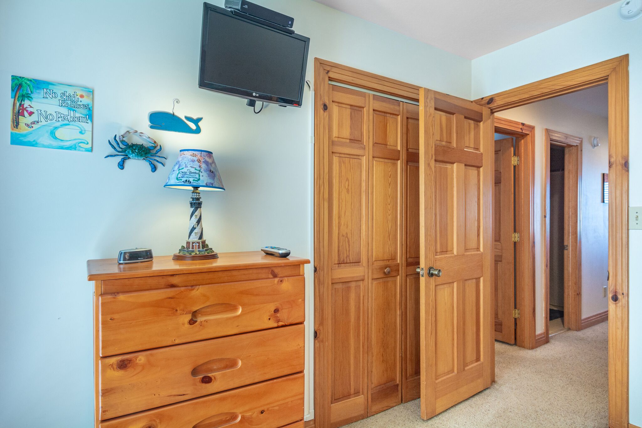 A room with a wooden dresser, a television mounted on the wall, and a door leading to another room.