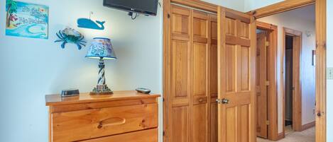 A room with a wooden dresser, a television mounted on the wall, and a door leading to another room.