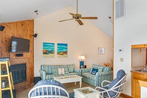 Ein gemütliches Wohnzimmer mit Kamin, gestreifte Sofas, einem weißen Couchtisch und einem Deckenventilator.