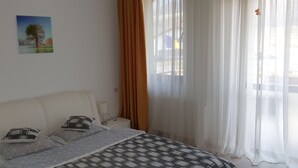 A bedroom with a bed, pillows, a bedside table with a lamp, and a window with sheer curtains. - Pensiunea Caraiman (Codlea)