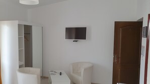 A room with a white wardrobe, a TV mounted on the wall, a small table with a remote control, and two chairs. - Pensiunea Caraiman (Codlea)