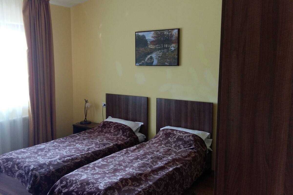 A room with two beds, a nightstand, a lamp, and a painting on the wall.