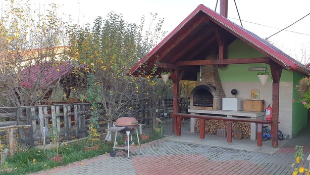 A brick patio with a barbecue grill, a stone fireplace, and a wooden fence. - Pensiunea Caraiman (Codlea)