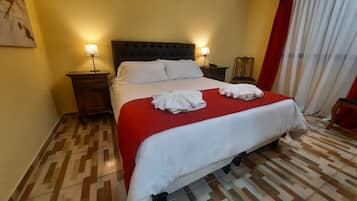 A hotel room with a bed, two bedside tables, a chair, and a window with curtains.