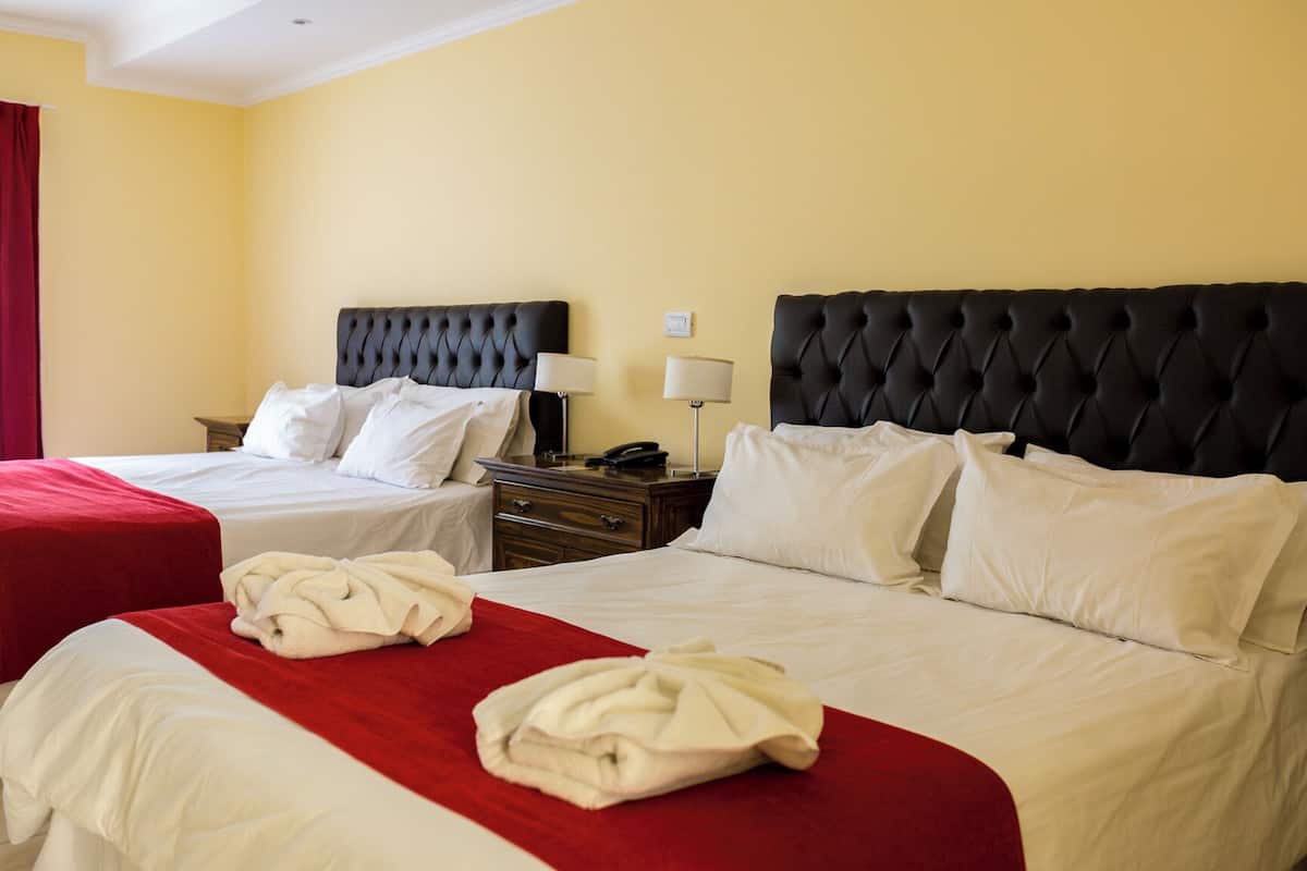 Une chambre d’hôtel avec deux lits, chacun recouvert d’une couvre-lit rouge et blanche, et dotée d’une tête de lit noire à motifs. Une table de chevet avec une lampe et un téléphone se trouve entre les deux lits.