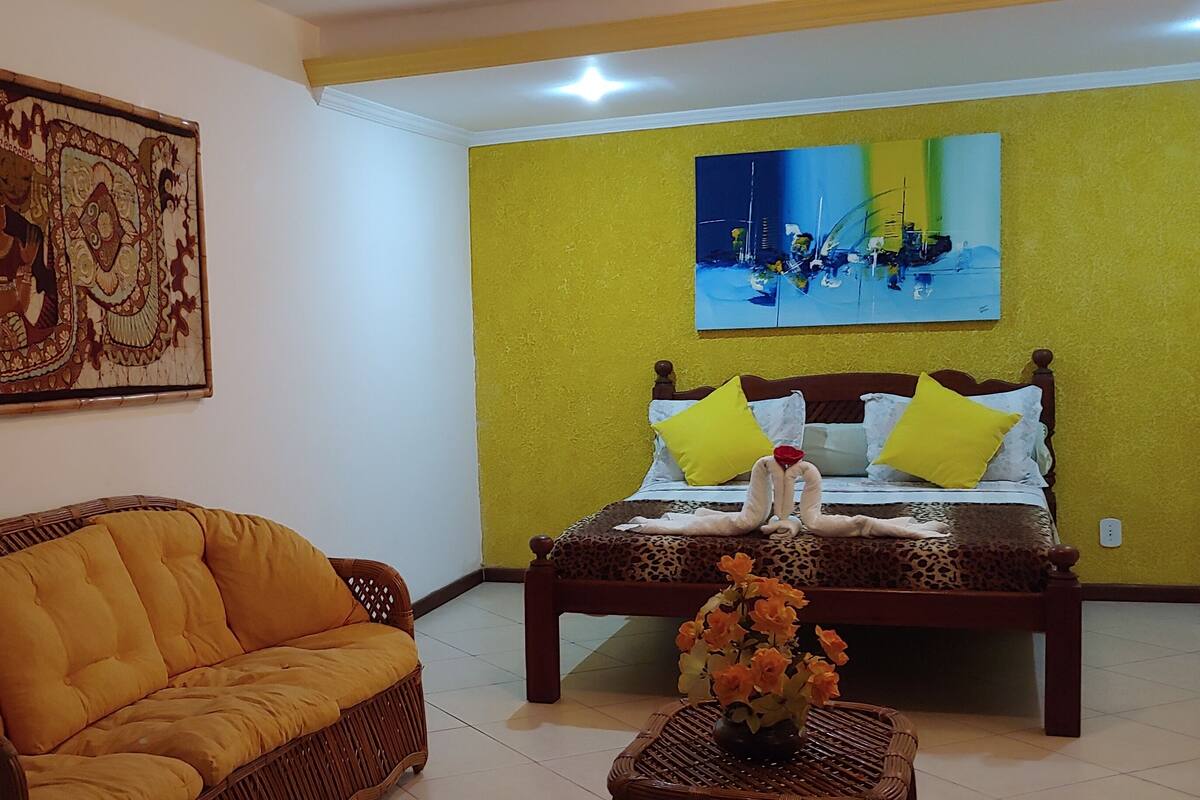 Una habitación con una cama, un sofá de mimbre, un cuadro en la pared y una pintura moderna.