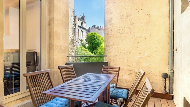 A balcony with a wooden table and chairs, a view of buildings, and a door to the left.