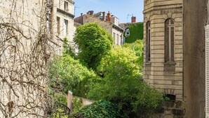 A narrow street with old stone buildings, one with a large tree in front.