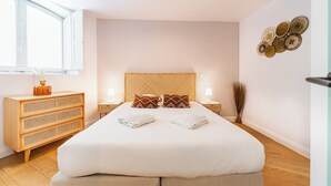 A modern bedroom with a large bed, two bedside tables with lamps, a wooden dresser, and decorative wall art.