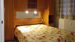 Un dormitorio con cabecera de madera, cama con edredón floral, espejo y radiador.