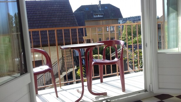 Un balcón con una mesa y dos sillas, con vista a una zona residencial con casas y cielo despejado.