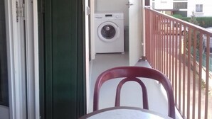 Un balcón con lavadora, una mesa y una silla.