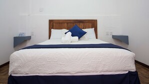 A neatly made bed with a wooden headboard, white linens, and a blue pillow. There are two bedside tables with water bottles on them. - Hotel Casa de las Piedras (Querétaro)