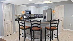 Una cocina moderna con armarios blancos, una isla central con taburetes y electrodomésticos de acero inoxidable.