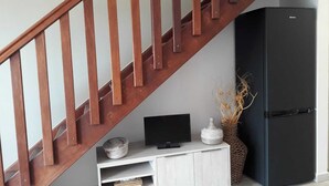 A staircase with wooden balusters, a white console table with a flat-screen TV, a black refrigerator, and decorative vases. - Charming duplex with no water shut-off (Le Gosier)
