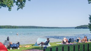 Un campamento junto al lago con tiendas de campaña, sillas y gente relajándose junto al agua.