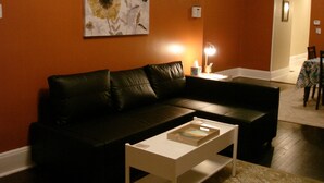 A living room with a black leather sofa, a white coffee table, and a painting of flowers on the wall.