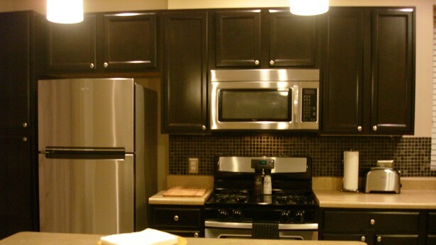 A modern kitchen with dark cabinets, stainless steel appliances, and a wooden island with a cutting board.
