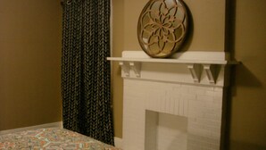 A bedroom with a patterned bedspread, a decorative wall piece above a fireplace, and a patterned curtain.
