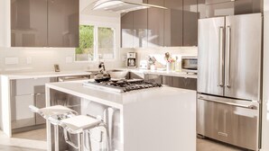 A modern kitchen with a central island, stainless steel appliances, and a large window providing natural light. - For The Record (Palm Springs)