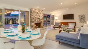 Ein modernes Wohnzimmer mit Kamin aus Stein, einem Essbereich mit weißen Stühlen und blauen Platzsets sowie einem blauen Sofa.
