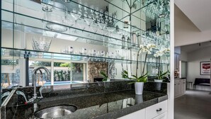 Eine moderne Küche mit einer Granitabdeckung, einer Edelstahlspüle und einer großen Glasrückwand mit verschiedenen Gläsern.
