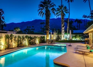 A swimming pool with a view of mountains at dusk, surrounded by palm trees and a patio area with lounge chairs. - Movie Colony Palms (Palm Springs)