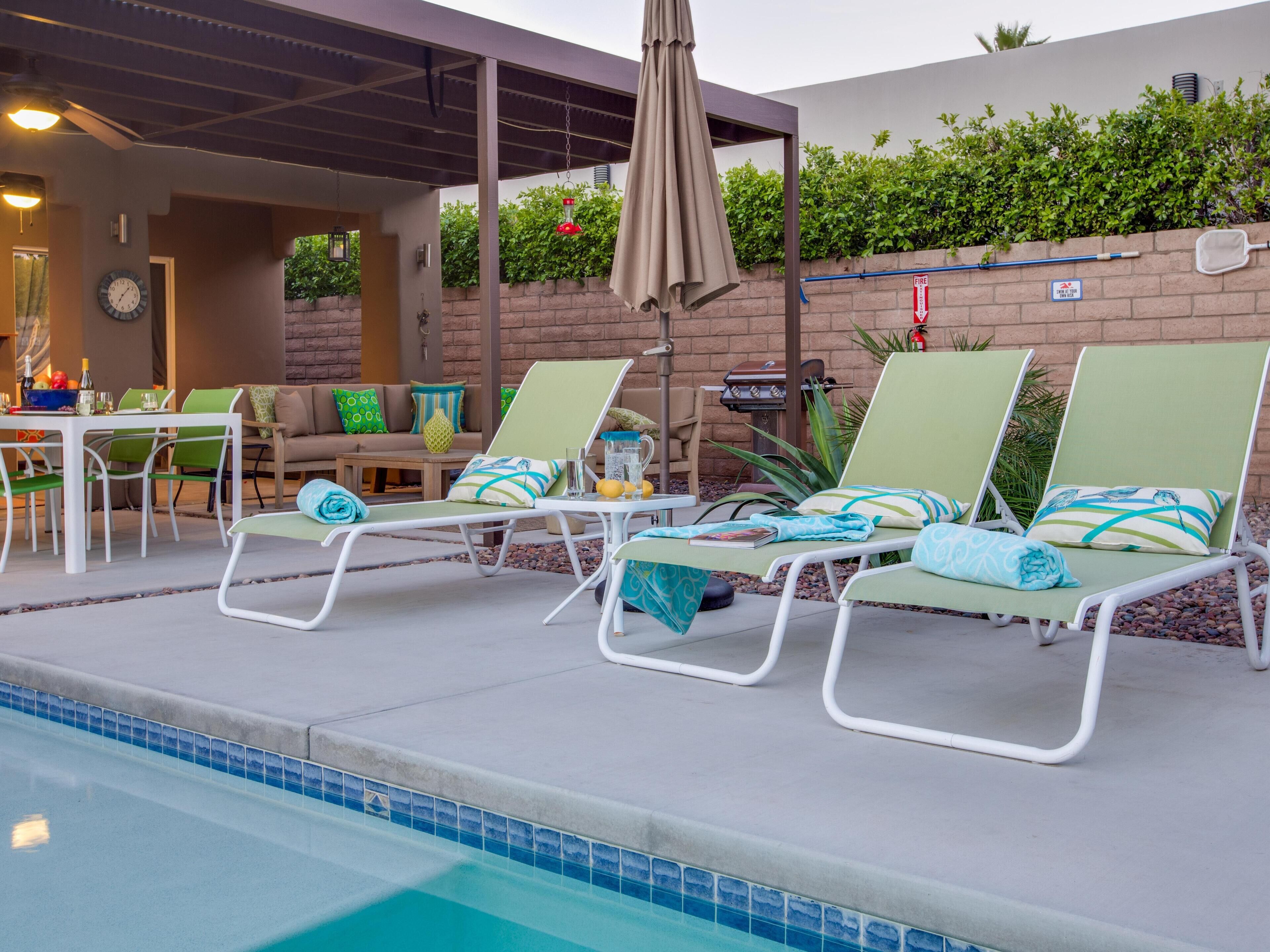 A poolside area with lounge chairs, a table with drinks, and a barbecue grill.