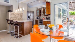 A modern kitchen with a central island, stainless steel appliances, and a dining area with orange chairs and a glass table. - San Lucas Hideout (Palm Springs)