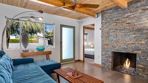 A modern living room with a stone fireplace, a blue sofa, a wooden coffee table, and a ceiling fan.