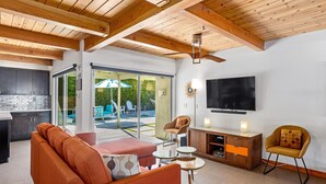 A modern living room with a sofa, coffee table, and armchairs, a TV, and a wooden ceiling.