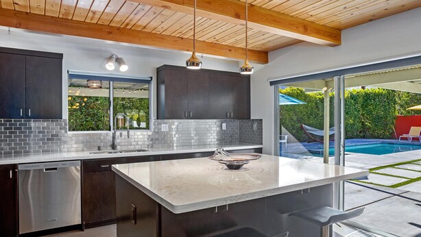 A modern kitchen with dark cabinets, a stainless steel dishwasher, and a large island with bar stools.
