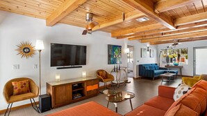A modern living room with wooden beams, a TV, a sofa, chairs, and a coffee table.