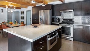 A modern kitchen with dark cabinetry, stainless steel appliances, and a marble countertop.