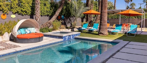 A swimming pool with a built-in hot tub, surrounded by lounge chairs and umbrellas.