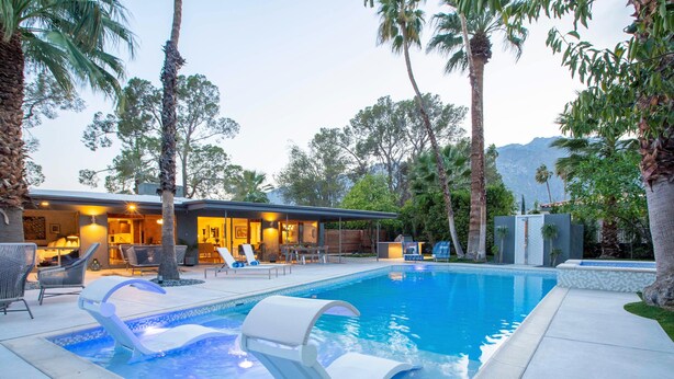 A swimming pool with lounge chairs, a covered patio area, and a modern house in the background.