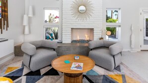 A modern living room with a fireplace, two grey armchairs, a round wooden coffee table, and a geometric patterned rug. - Mid Mod Sunsation (Palm Springs)