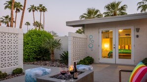 A modern outdoor patio with a fire feature, seating, and a view of a bedroom with a bed and curtains. - Mid Mod Sunsation (Palm Springs)