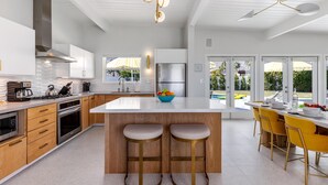 A modern kitchen with a central island, wooden cabinets, stainless steel appliances, and a dining area with yellow chairs. - Mid Mod Sunsation (Palm Springs)
