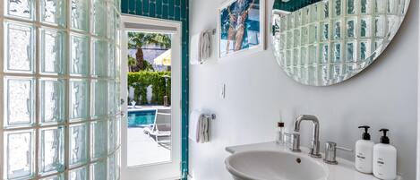 Un bany amb una gran porta de vidre, un lavabo blanc amb un mirall a sobre i dues ampolles de sabó de mans i loció al lavabo.
