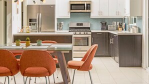 A modern kitchen with white cabinets, stainless steel appliances, and a central island with seating. - Alexander Sunrise (Palm Springs)