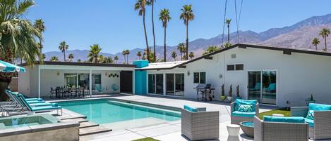A modern house with a swimming pool, outdoor furniture, and palm trees.