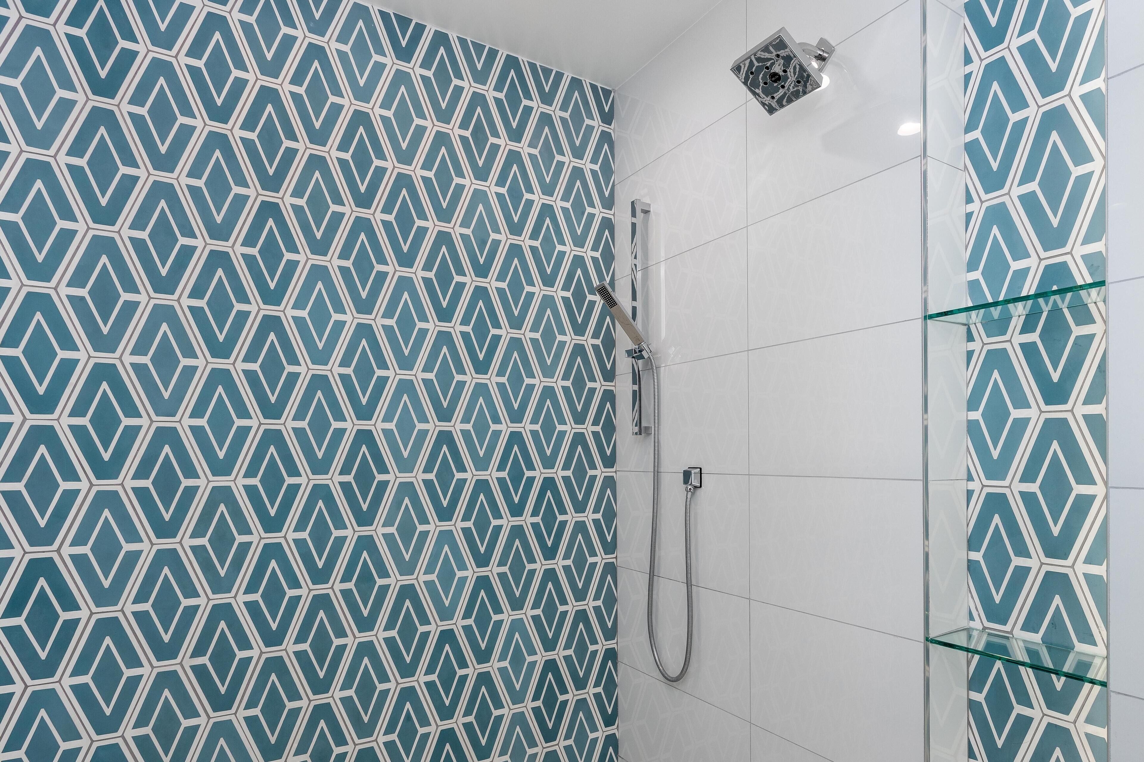 Un baño con pared de azulejos de diseño geométrico, cabina de ducha de vidrio y ducha de mano.