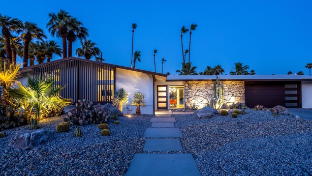 A modern house with a stone facade, a wooden deck, and a gravel driveway. - Alexander Sunrise (Palm Springs)