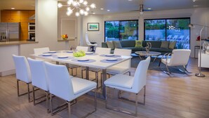 A modern living area with a dining table, white chairs, a sofa, and a balcony with a view. - Mid-century Deluxe (Palm Springs)