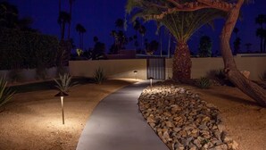 A nighttime outdoor pathway with a palm tree and a rock garden. - Mid-century Deluxe (Palm Springs)