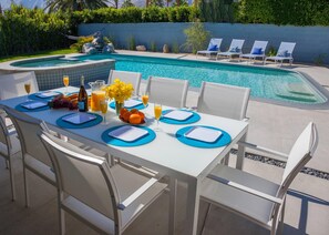A poolside dining area with a table set for two, surrounded by white chairs. - Mid-century Deluxe (Palm Springs)
